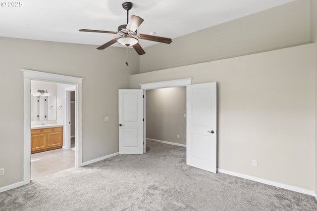 unfurnished bedroom featuring a ceiling fan, light colored carpet, a sink, baseboards, and ensuite bathroom
