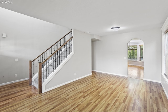 unfurnished living room with stairway, baseboards, and wood finished floors