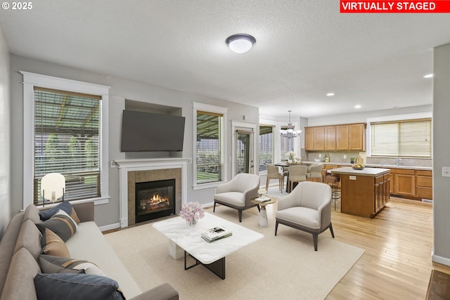 living area with an inviting chandelier, recessed lighting, a textured ceiling, a tile fireplace, and light wood-style flooring