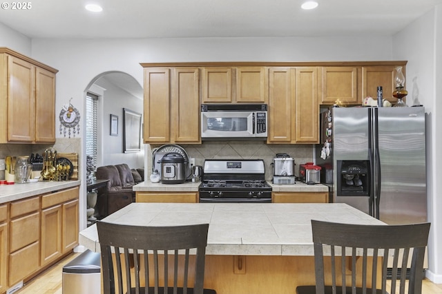 kitchen with a breakfast bar area, tile countertops, decorative backsplash, and appliances with stainless steel finishes