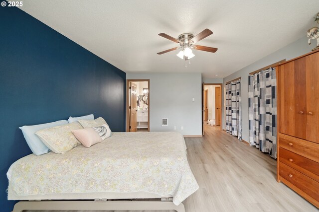 bedroom featuring light wood-type flooring, a ceiling fan, ensuite bath, and visible vents