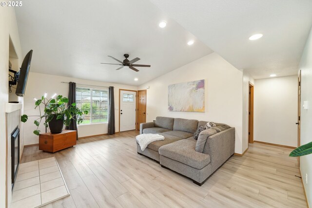 living room featuring a ceiling fan, vaulted ceiling, light wood finished floors, and a fireplace