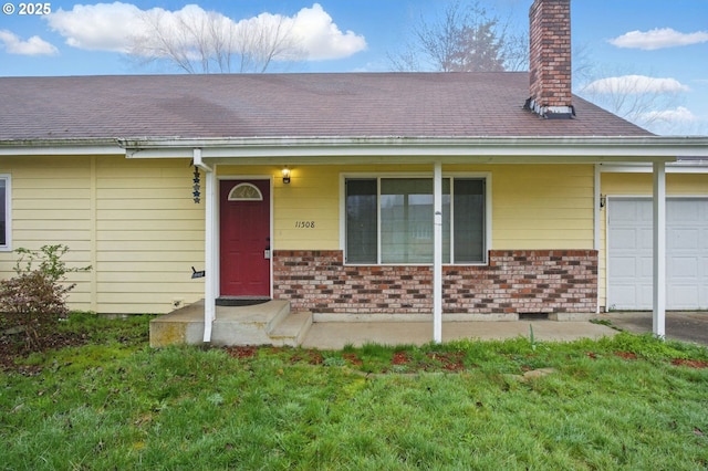 view of exterior entry featuring a yard, brick siding, an attached garage, and a chimney