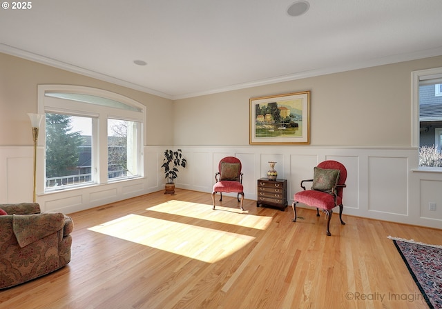 living area featuring crown molding, a decorative wall, wood finished floors, and wainscoting