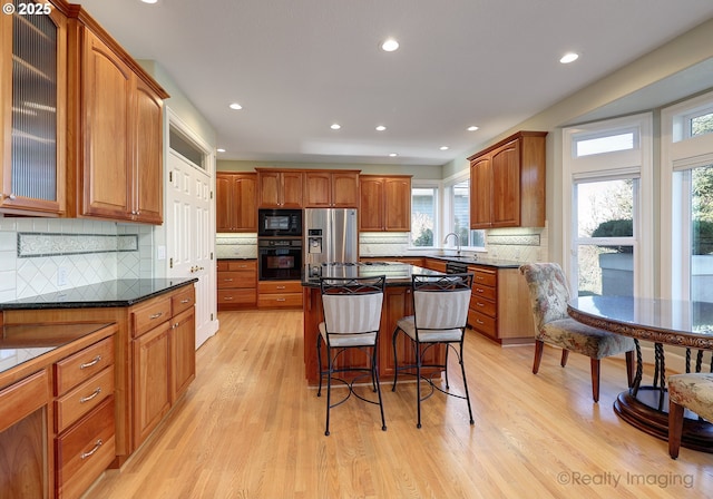 kitchen featuring a breakfast bar, a center island, glass insert cabinets, light wood-style floors, and black appliances