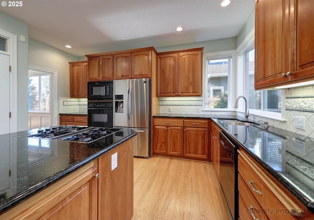 kitchen featuring black appliances, dark stone counters, a sink, and brown cabinetry