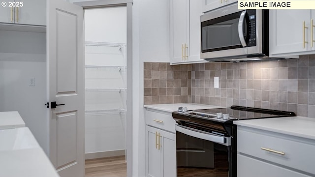 kitchen featuring light countertops, stainless steel microwave, white cabinets, and black electric range oven