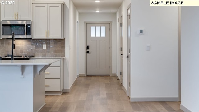 kitchen featuring stainless steel microwave, a breakfast bar, light countertops, light wood-type flooring, and white cabinetry