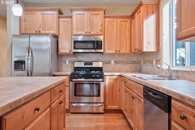 kitchen featuring tile counters, decorative backsplash, stainless steel appliances, light wood-style floors, and a sink