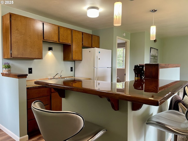 54825 Robinson Rd, Coquille, OR 97423 - kitchen featuring freestanding refrigerator, wood finished floors, brown cabinetry, a breakfast bar, and hanging light fixtures