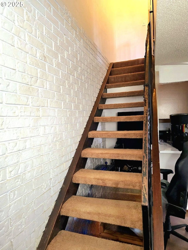 stairway featuring a textured ceiling and brick wall