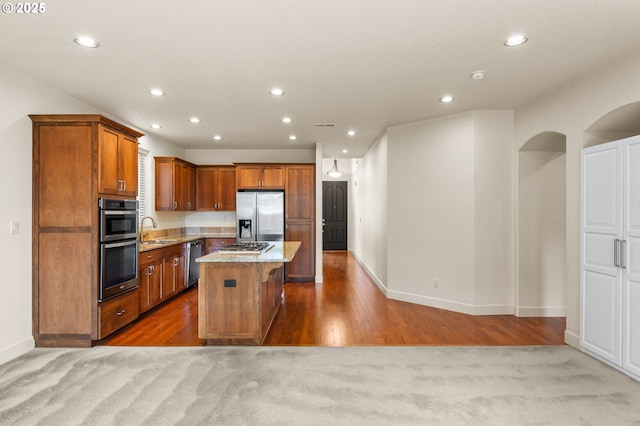 kitchen with appliances with stainless steel finishes, a sink, a kitchen island, baseboards, and brown cabinets
