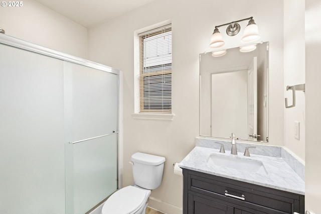 bathroom featuring toilet, a stall shower, vanity, and baseboards