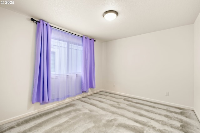 empty room with carpet, baseboards, and a textured ceiling