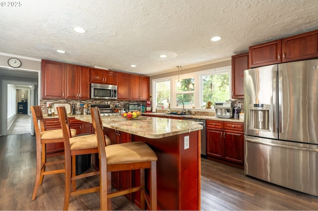 kitchen with appliances with stainless steel finishes, a sink, reddish brown cabinets, tasteful backsplash, and dark wood-style floors