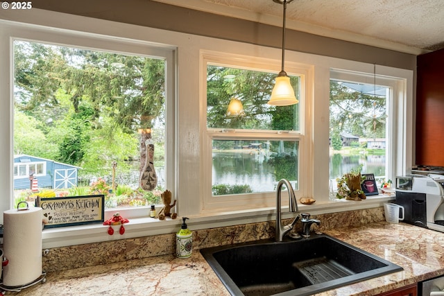 kitchen featuring a sink, pendant lighting, a textured ceiling, and light stone countertops