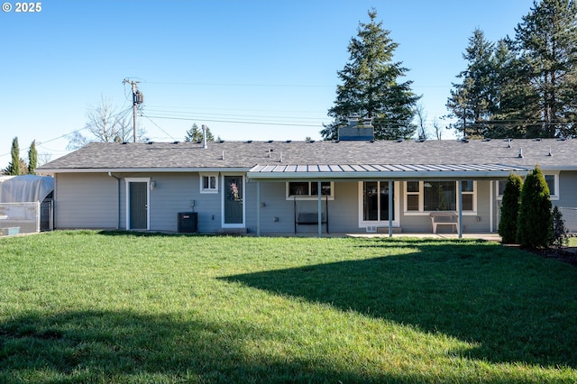 rear view of house featuring a chimney, a lawn, central AC unit, a standing seam roof, and metal roof