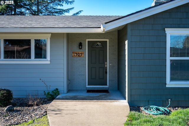 entrance to property with a shingled roof and brick siding