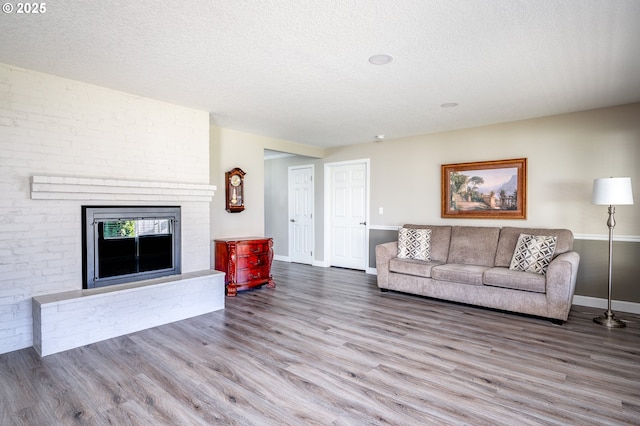 living room featuring hardwood / wood-style floors, a textured ceiling, and a brick fireplace