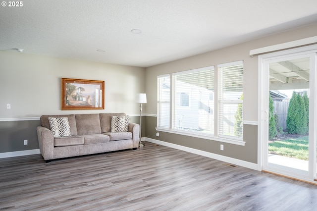 living room with a textured ceiling, wood finished floors, visible vents, and baseboards