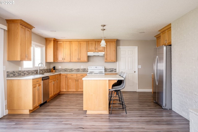 kitchen with a breakfast bar area, under cabinet range hood, stainless steel appliances, a sink, and light countertops