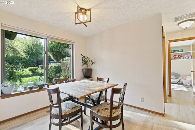 dining area with baseboards, light wood-style flooring, a textured ceiling, and visible vents