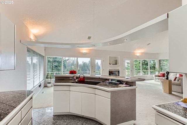 8408 NW Pinnacle Ct, Portland, OR 97229 - kitchen with open floor plan, white cabinets, a tiled fireplace, a sink, and high vaulted ceiling