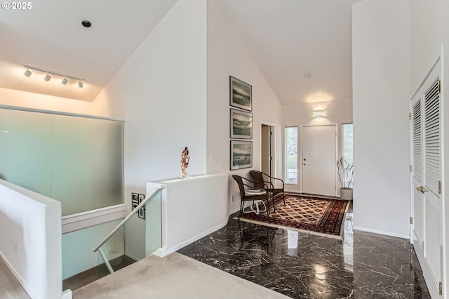 entryway with track lighting, baseboards, marble finish floor, and high vaulted ceiling