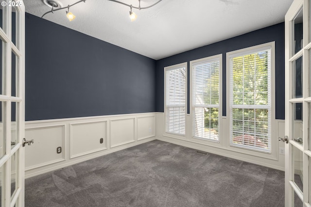 6783 Apollo Rd, West Linn, OR 97068 - empty room featuring wainscoting, french doors, dark carpet, a decorative wall, and a textured ceiling