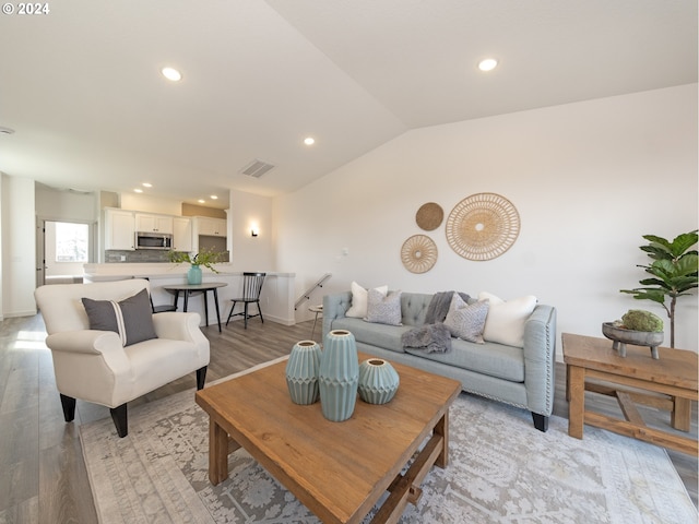 living room with light wood-style flooring, visible vents, vaulted ceiling, and recessed lighting