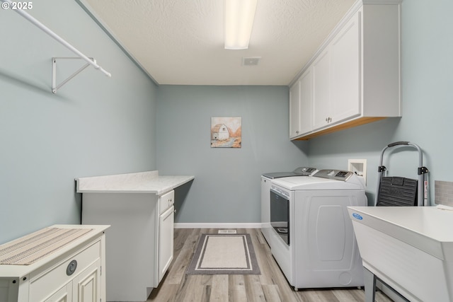 washroom featuring cabinets, a textured ceiling, sink, light hardwood / wood-style flooring, and washing machine and clothes dryer