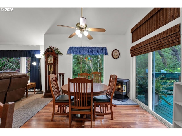 dining space featuring a wood stove, ceiling fan, wood finished floors, and a healthy amount of sunlight