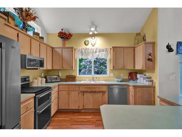 kitchen with a sink, light brown cabinets, stainless steel appliances, and light wood finished floors