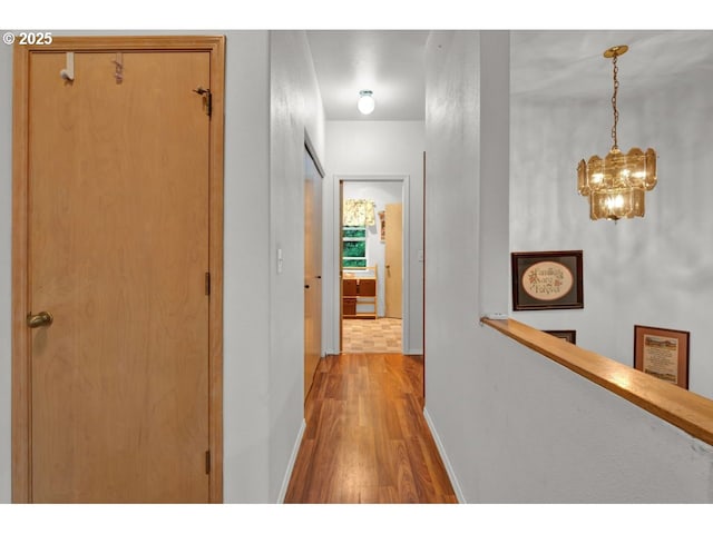hall featuring baseboards, light wood-style flooring, an upstairs landing, and an inviting chandelier