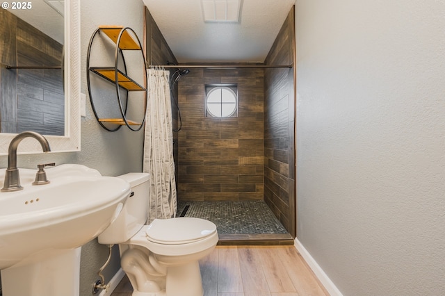 bathroom featuring a textured wall, toilet, a sink, wood finished floors, and a shower stall