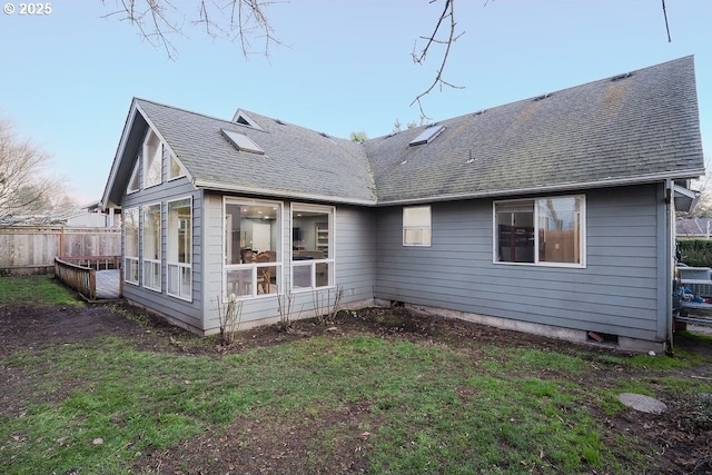 back of house featuring a shingled roof, fence, and a lawn