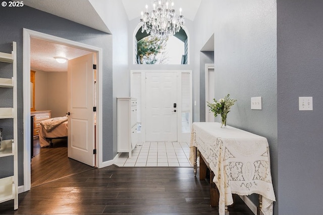 entrance foyer featuring a textured wall, high vaulted ceiling, wood finished floors, and a notable chandelier