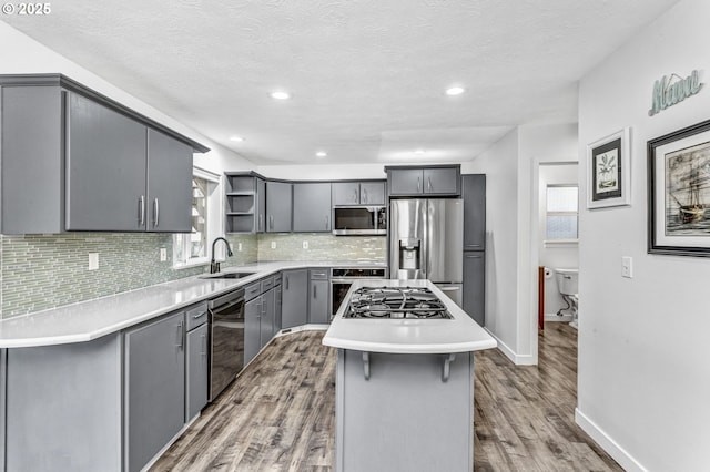 kitchen with backsplash, open shelves, gray cabinets, stainless steel appliances, and a sink