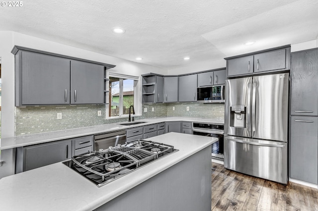 kitchen with gray cabinets, a sink, open shelves, appliances with stainless steel finishes, and dark wood-style flooring