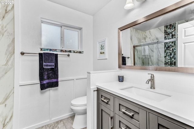 full bath with a wainscoted wall, toilet, a marble finish shower, a decorative wall, and vanity