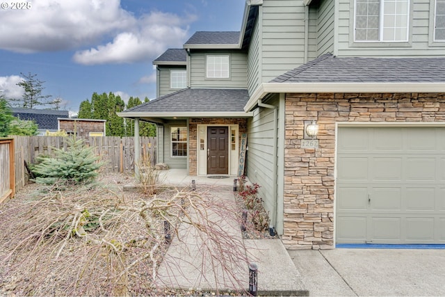 property entrance with stone siding, a shingled roof, a garage, and fence