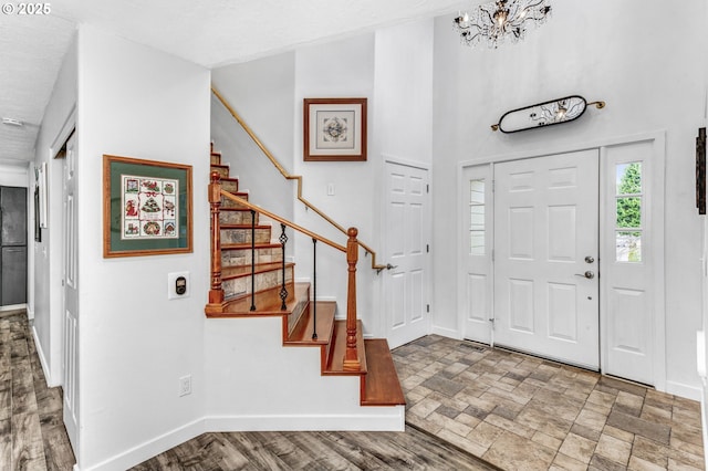 foyer entrance featuring a notable chandelier, stone finish floor, stairs, and baseboards