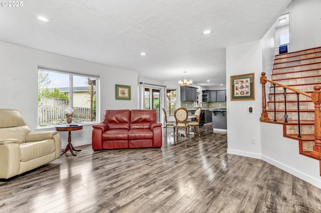 living room featuring a wealth of natural light, stairway, an inviting chandelier, and wood finished floors