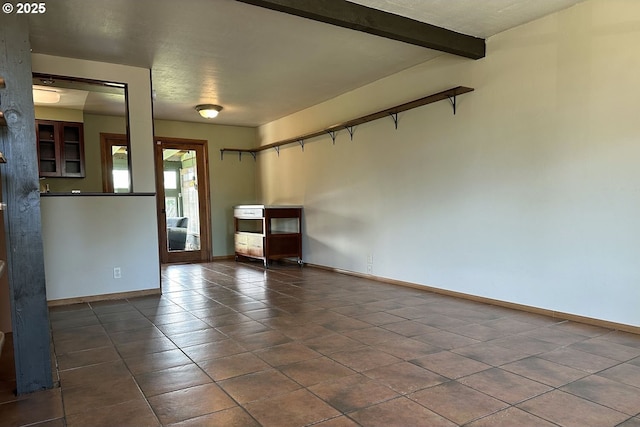 unfurnished living room with baseboards, dark tile patterned floors, and beam ceiling