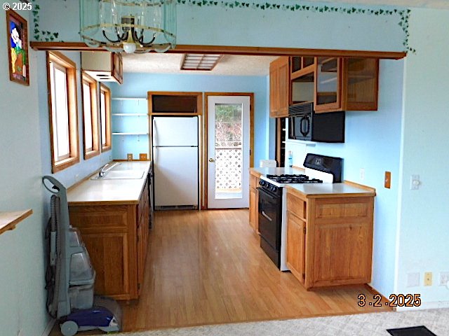 kitchen with light wood-type flooring, black appliances, glass insert cabinets, and light countertops