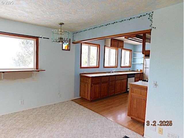 kitchen featuring light countertops, stainless steel dishwasher, freestanding refrigerator, brown cabinetry, and an inviting chandelier