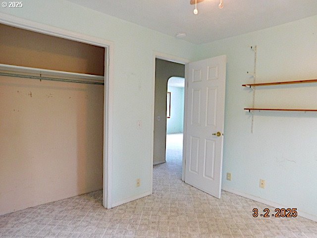 unfurnished bedroom with arched walkways, a closet, and light colored carpet