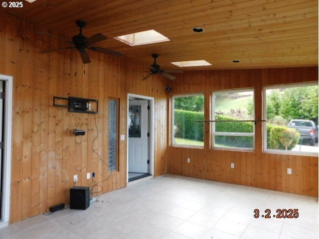 empty room featuring ceiling fan, wooden walls, vaulted ceiling with skylight, wooden ceiling, and tile patterned floors