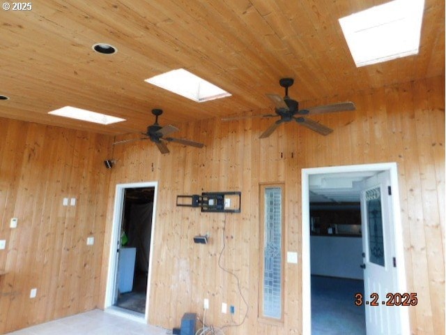 empty room with a skylight, wooden ceiling, ceiling fan, and wooden walls