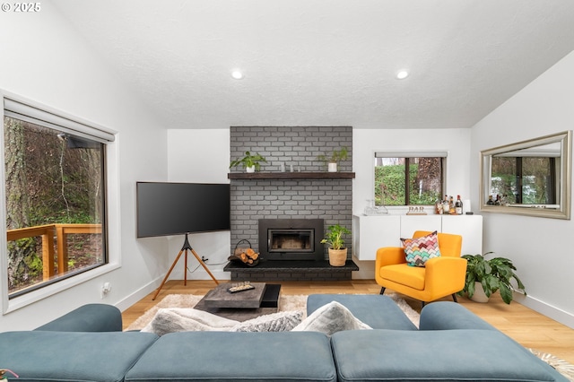 living room featuring lofted ceiling, a brick fireplace, light hardwood / wood-style flooring, and a textured ceiling